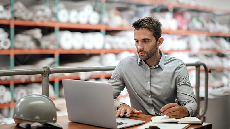 Warehouse manager taking notes and checking orders with a laptop 