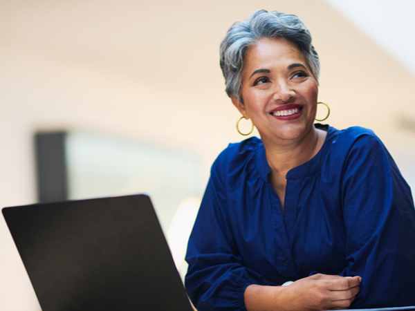Smiling senior woman gazes thoughtfully away from her laptop.