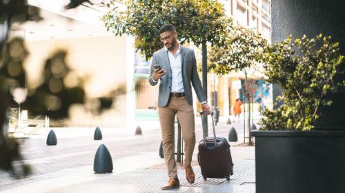 person looking at phone walking down the sidewalk with luggage