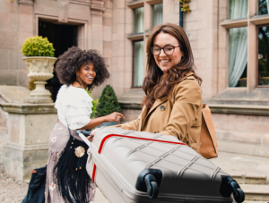 Two friends arrive at a luxury hotel where they are unloading their suitcases from their car trunk.