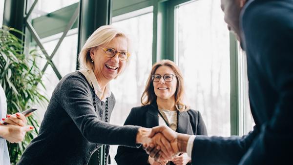 woman shaking hands with man as another woman looks on